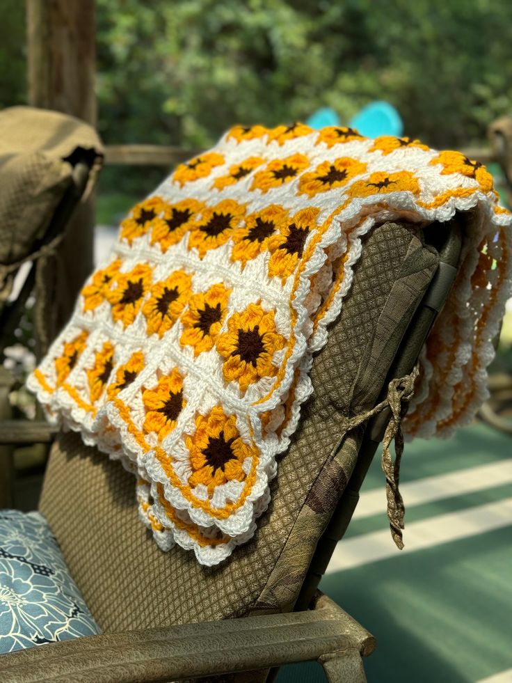 a crocheted sunflower blanket sitting on top of a wooden chair next to pillows