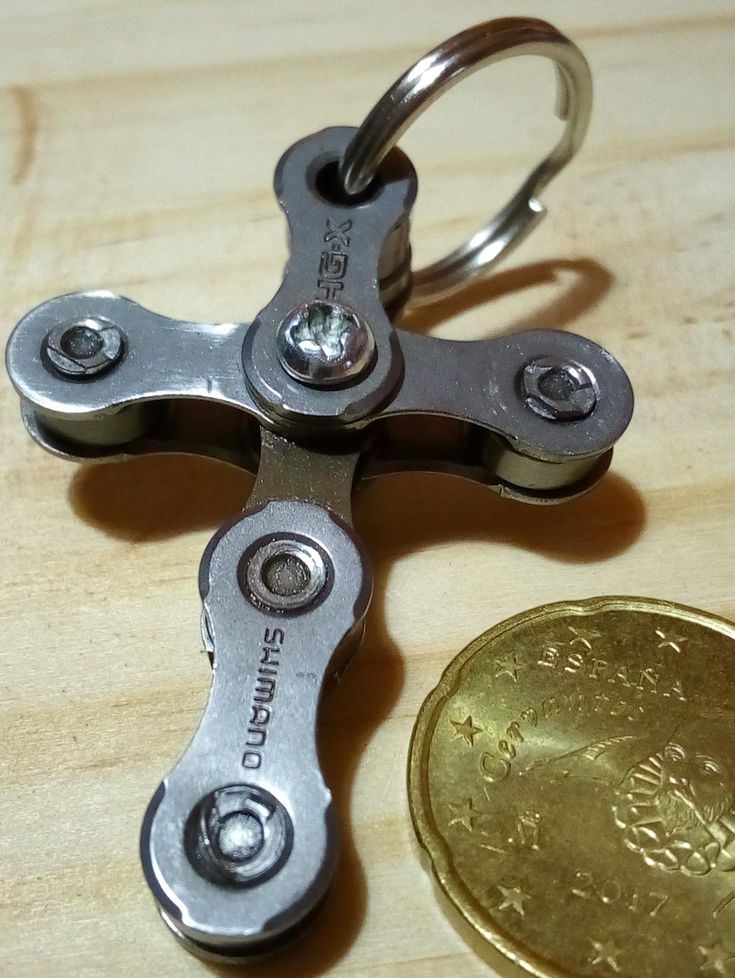 a metal cross shaped keychain sitting next to a coin on a wooden surface