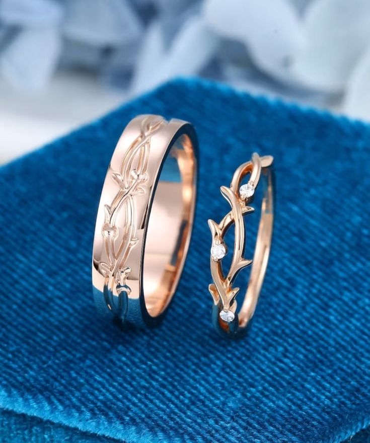 two gold wedding rings sitting on top of a blue cloth