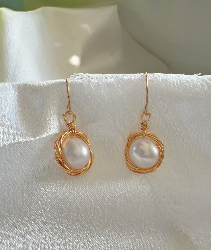 Experience the blend of traditional elegance and modern craftsmanship with our Handcrafted Wire-Wrapped Pearl Earrings. Each earring features a lustrous pearl encased in a delicate gold wire nest, offering a unique and stylish look. These earrings are perfect for those who appreciate the beauty of handcrafted jewelry and seek a versatile accessory that pairs well with both formal and casual outfits. Features: Material: High-quality pearl and gold-colored wire Design: Unique wire nest design arou Elegant Gold-tone Earrings For Anniversary, Rose Gold Metal Pearl Earrings For Gifts, Classic Gold Wrap Earrings, Rose Gold Pearl Earrings As Gift, Elegant Metal Earrings For Gift, Gold Drop Pearl Earrings For Gift, Elegant Gold-tone Hoop Earrings, Elegant Round Wire Wrapped Jewelry, Dainty Gold Earrings With Elegant Design