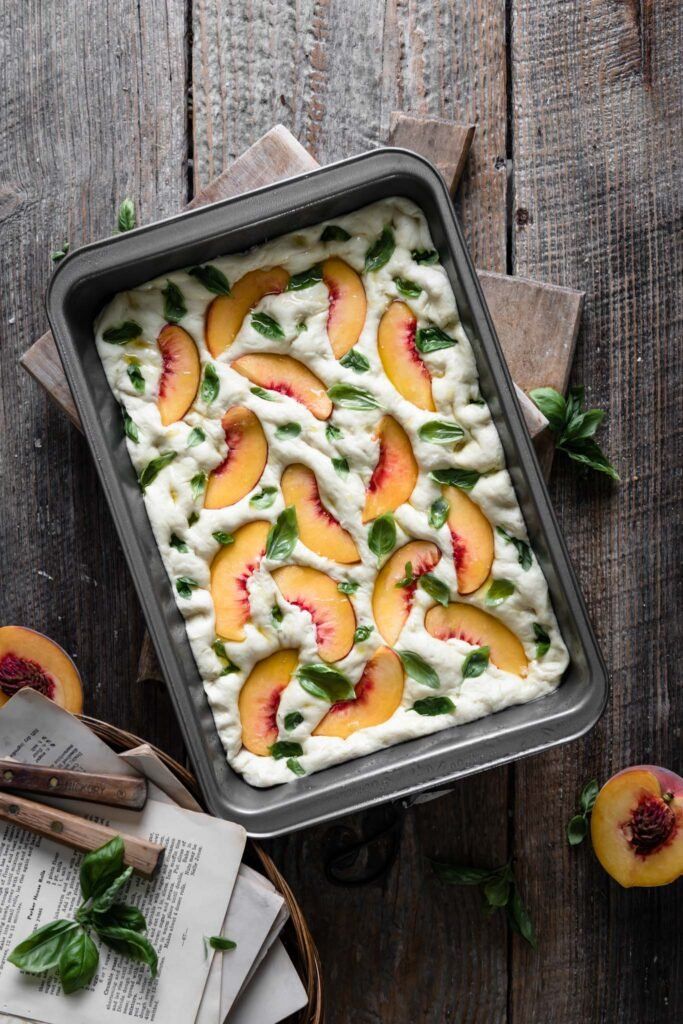 peaches and whipped cream in a baking pan on a wooden table with spoons