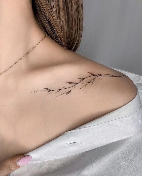 the back of a woman's shoulder with a small branch tattoo on it