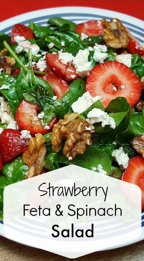 a salad with strawberries, feta and spinach on it in a blue and white plate