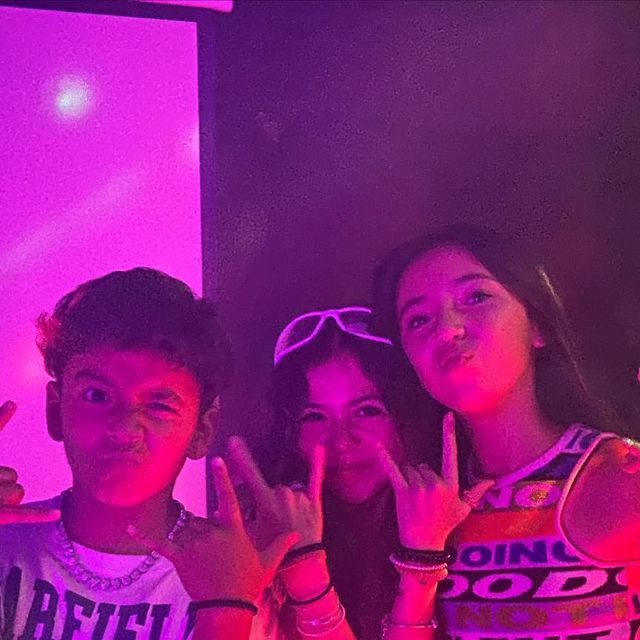 three young people posing for the camera in front of a purple light with their hands up