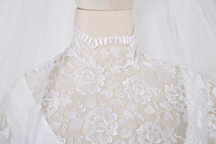 the back of a wedding dress with white lace and flowers on it's neck