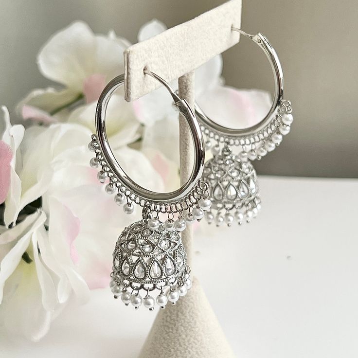 "These silver-plated polki chandbali jhumka hoop earrings are a stunning addition to any outfit. The intricate detailing and silver beads add an elegant touch to this Bollywood inspired piece, while polki stones give it a gorgeous sparkle that's sure to catch light and make heads turn. Length 2.5\" | Width 1.5\" Items are carefully packed and ready for gifting. All pictures are taken in natural light please allow for slight variations in color due to camera settings. Jewelry Care ✨Protect your j Luxury Round Silver Jhumkas, Silver Hoop Jewelry For Celebration, Silver Bollywood Hoop Earrings With Intricate Design, Silver Metal Hoop Earrings For Celebrations, Bollywood Style Intricate Silver Hoop Earrings, Silver Hoop Bridal Earrings For Wedding, Festive Metal Hoop Earrings, Bollywood Silver Dangle Chandelier Earrings, Silver Bollywood Chandelier Dangle Earrings