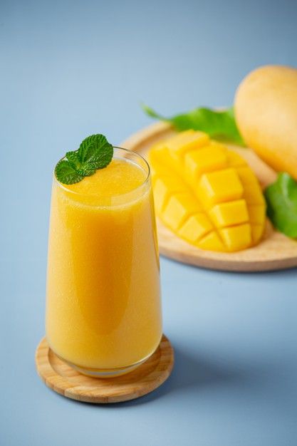 a glass of mango juice next to a wooden plate