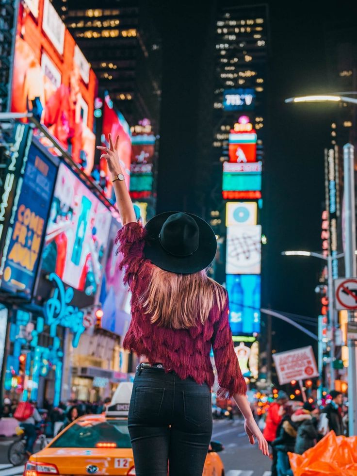 a woman standing in the middle of a busy city at night with her arms up