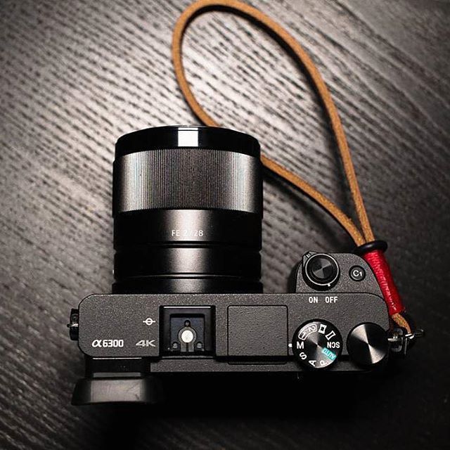 a camera sitting on top of a wooden table next to a brown cord with a red handle