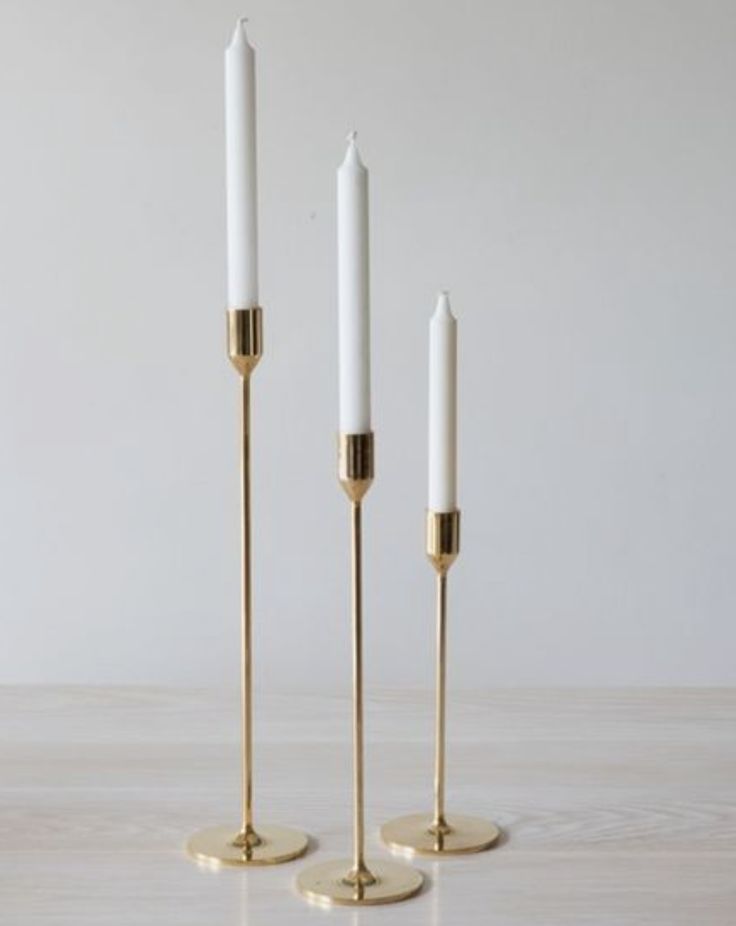 three white candles sitting on top of each other in front of a white wall and floor