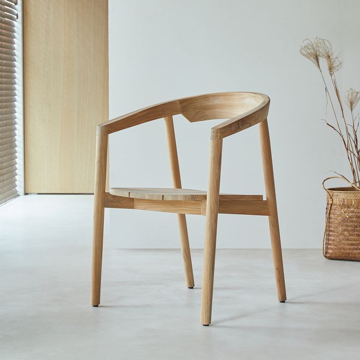 a wooden chair sitting in front of a window next to a basket with flowers on it