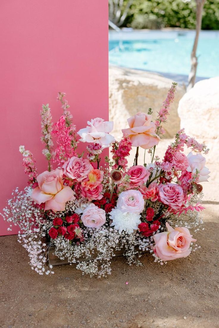 a vase filled with pink and white flowers next to a swimming pool in the background