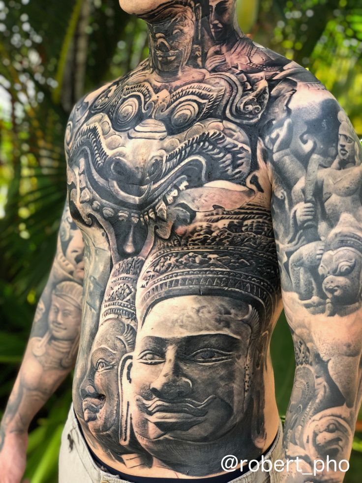 a man with many tattoos on his chest and back is standing in front of some trees