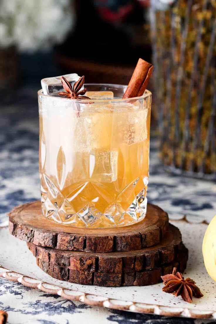 an old fashioned drink is sitting on a wooden coaster with cinnamon stick and star anise