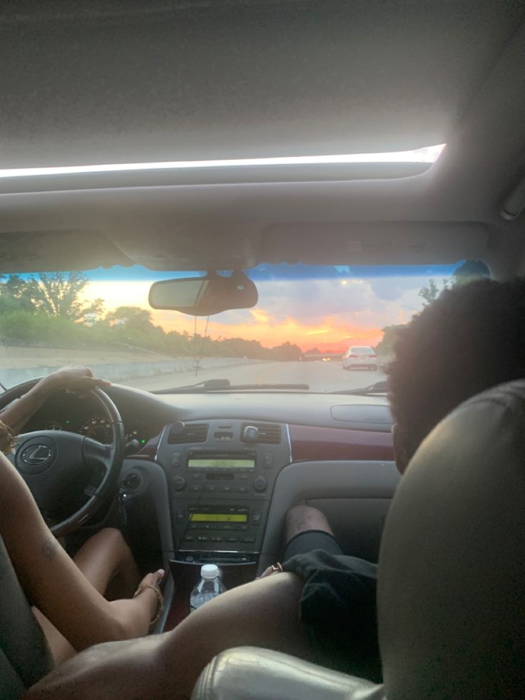 two people sitting in the driver's seat of a car at sunset or dawn