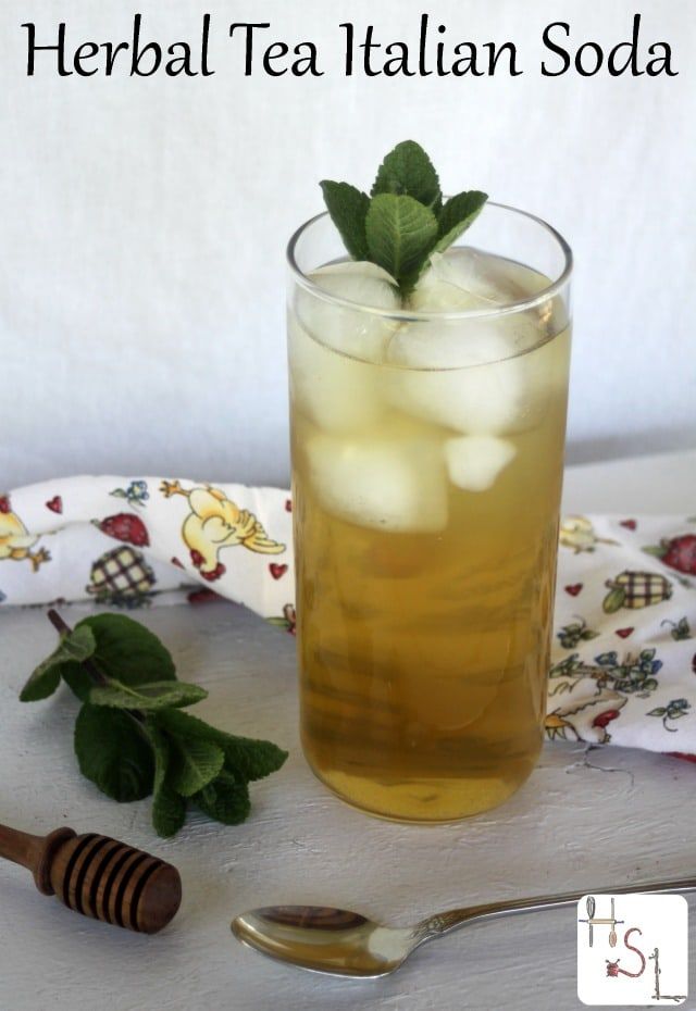 a glass filled with ice and mint tea next to a spoon on top of a table