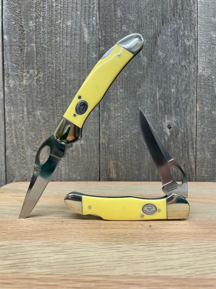 a pair of yellow and black scissors sitting on top of a wooden table next to each other