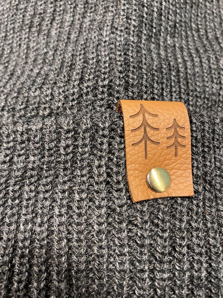 Give the gift of warmth and style! This knit beanie is perfect for hiking, camping, and perfect for keeping warm! Beanie is a dark charcoal gray color, and is made of a soft wool/acrylic blend. Attached is an engraved leather label tag with a brass rivet. The leather label is engraved on both sides, so whether you wear the hat with the brim up or down, the label will still show the design in the correct orientation. Choice of circle logo or trees available at checkout. Care - Hand wash, dry flat Warm Beanie For Outdoor Winter Wear, Warm Beanie For Outdoor Use, Black Winter Camping Hat, Gray Warm Beanie For Outdoor, Warm Gray Beanie For Outdoor, One Size Fits Most Beanie For Fall Outdoor Activities, Winter Beanie For Outdoor Wear, Winter Knitted Beanie For Outdoor, Knitted Beanie For Winter Outdoor Wear