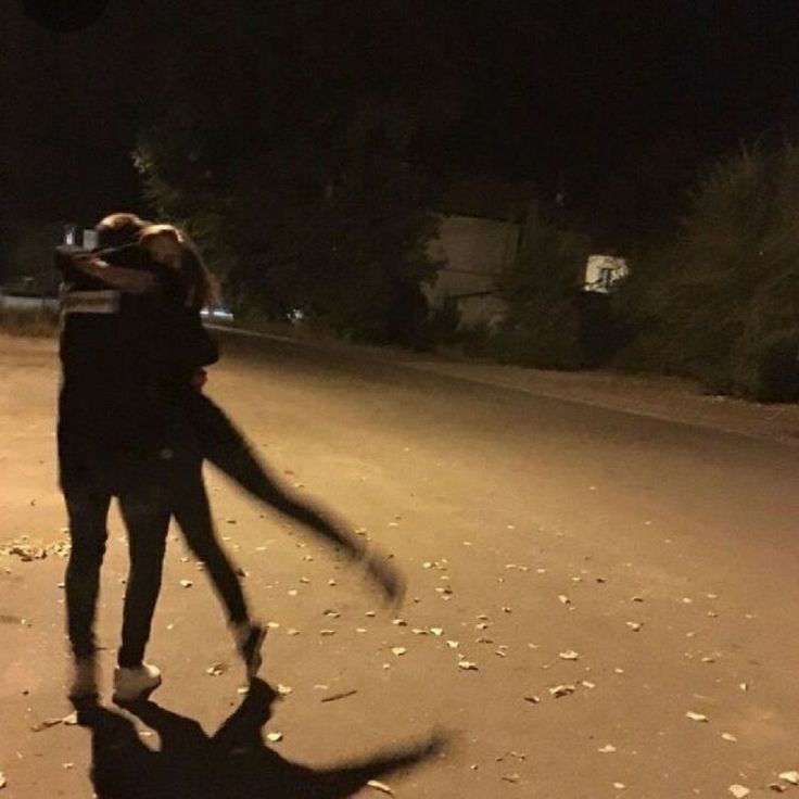 a man and woman walking down the street at night with their arms around each other