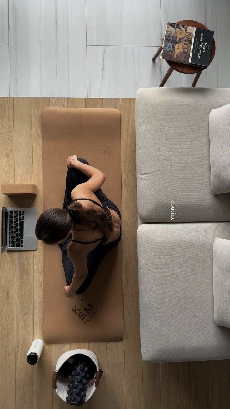 a woman sitting on top of a yoga mat in front of a laptop computer next to a couch