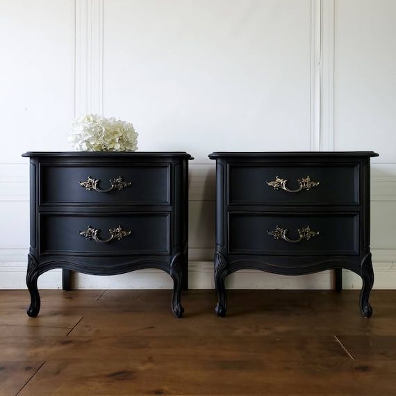 two black nightstands with gold handles on each side and white flowers on the top