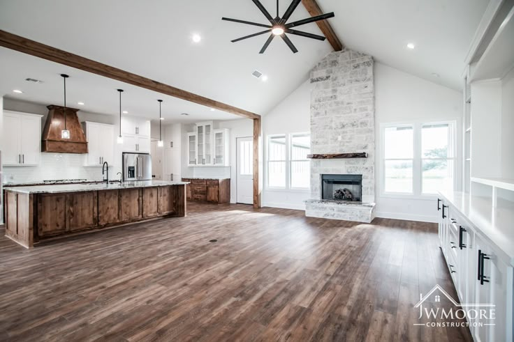 an empty kitchen and living room in a house with wood flooring, white walls, and exposed beams