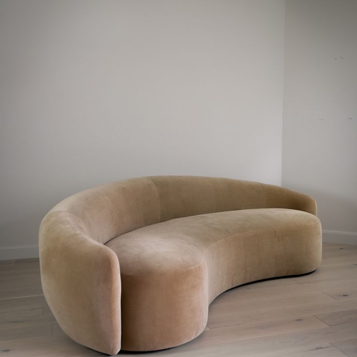 a curved couch sitting on top of a hard wood floor next to a white wall