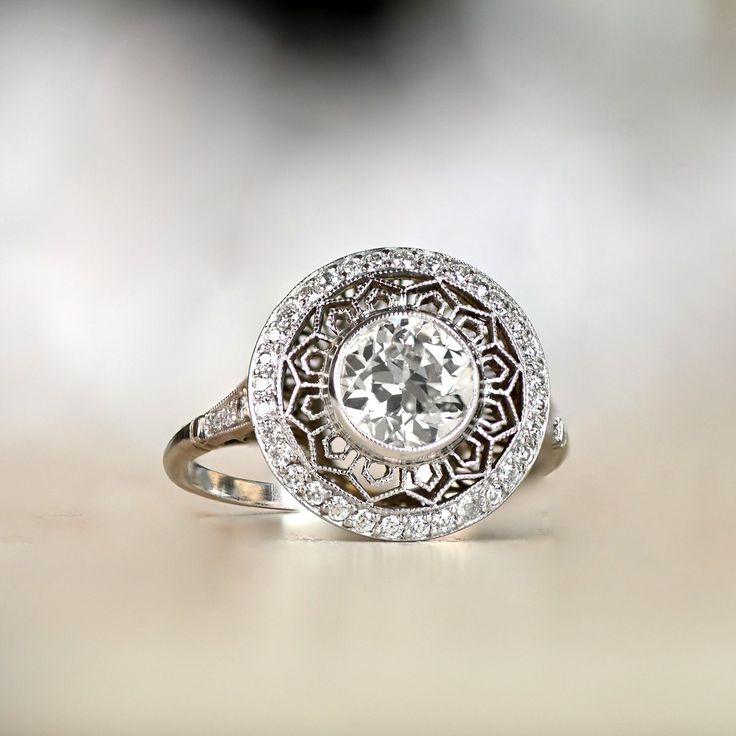 An Edwardian-inspired halo engagement ring featuring a bezel-set 1.12 carat old European cut diamond, J color and VS2 clarity. Beautiful lacey open-work connects the center diamond to the outer halo of old European cut diamonds. Additional diamonds are set along the shoulders. The under-gallery of this platinum ring is decorated with open-work. ✦ DIAMOND SPECIFICATIONS: Diamond Cut: Old European Cut Diamond Weight: 1.12 Carats Diamond Color: J Color Diamond Clarity: VS2 Clarity ✦ ENGAGEMENT RING Art Deco Diamond White Halo Ring With Center Stone, Art Deco Diamond Wedding Ring With Halo Setting, Art Deco Platinum Halo Ring With Center Stone, Vintage Diamond Cluster Ring With Halo, Art Deco Diamond White Rings With Halo Setting, Vintage White Wedding Ring With Halo Setting, White Vintage Wedding Ring With Halo Setting, Diamond White Halo Setting Art Deco Rings, Diamond White Art Deco Rings With Halo Setting