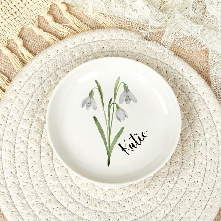 a plate with some flowers on it and the word kate written in black ink is sitting on a place mat