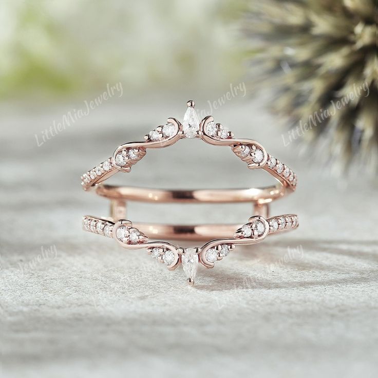 two rose gold wedding rings with diamonds on the top and bottom, sitting next to a pine cone