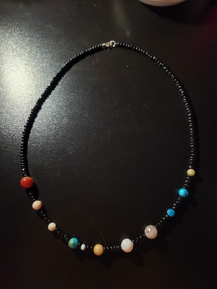 a black beaded necklace with multi - colored beads and silver clasp on a table