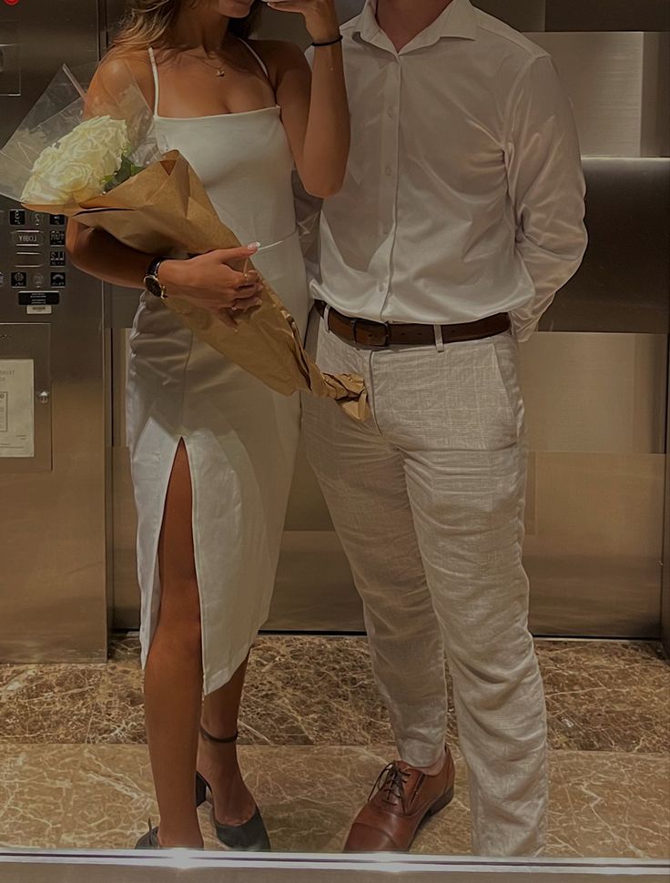 a man and woman standing next to each other in front of an elevator holding flowers