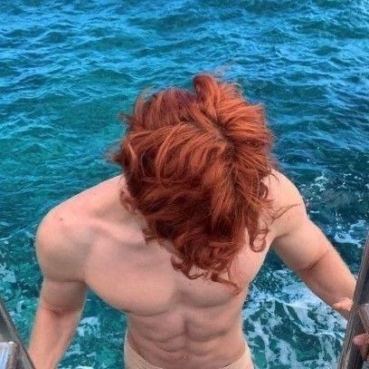 a shirtless man standing on the side of a boat looking out at the ocean