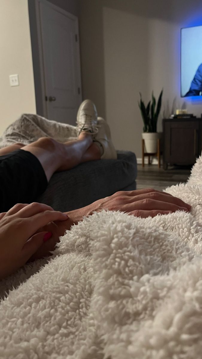 two people are sitting on a couch watching tv with their feet up in the air