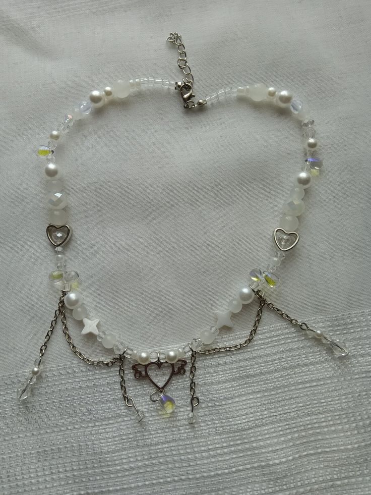 a white bracelet with charms and hearts on the clasp is laying on a bed sheet