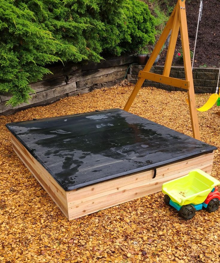 a child's play area with a swing set, sandbox and toy cars