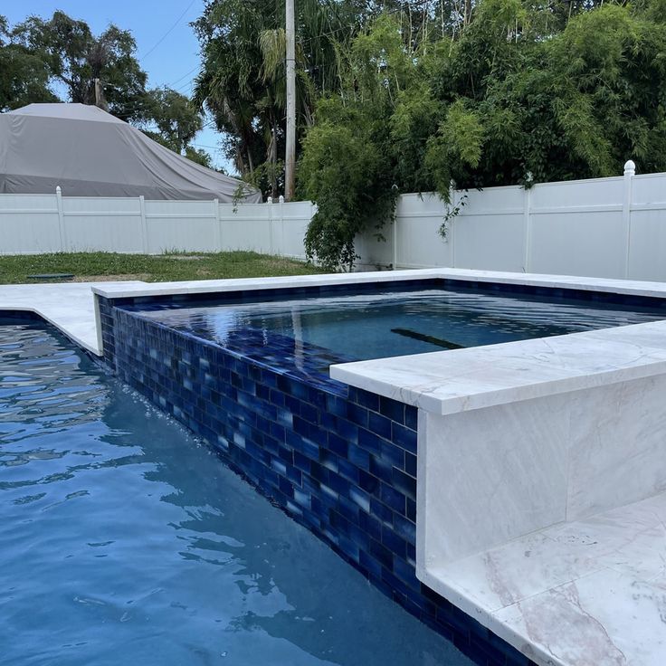 an empty swimming pool with blue tiles on the sides and white fence in the background