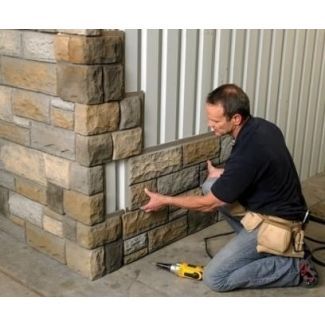 a man that is kneeling down next to a wall with some tools in his hand