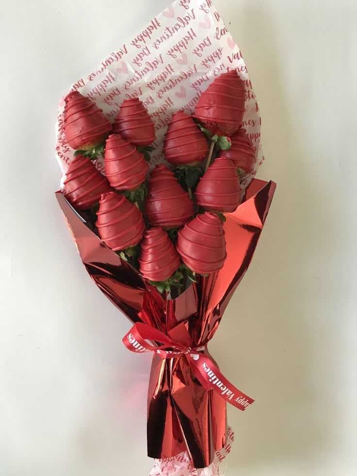 a bunch of chocolate covered strawberries wrapped in red paper and tied with a ribbon