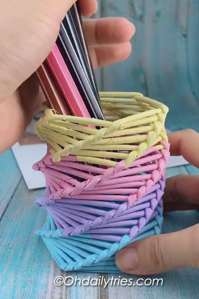 a person is holding a small basket made out of colored paper and some scissors in it