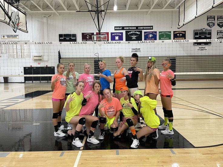 a group of young women standing on top of a gym floor holding volleyball racquets