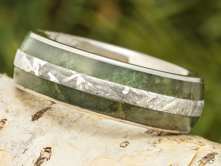 a wedding band with green and silver inlays sits on top of a tree trunk