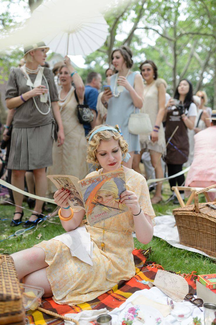 a woman sitting on the ground reading a book with other people standing around her and holding umbrellas