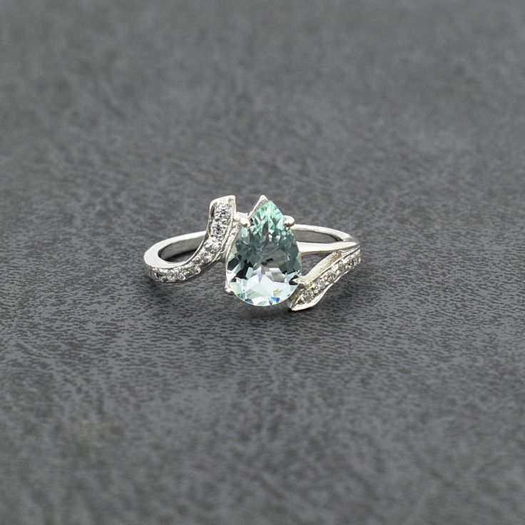 an aqua and white topazte ring with diamond accents on a gray tablecloth