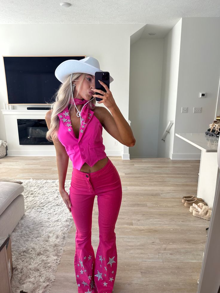 a woman taking a selfie in her living room wearing pink pants and cowboy hat