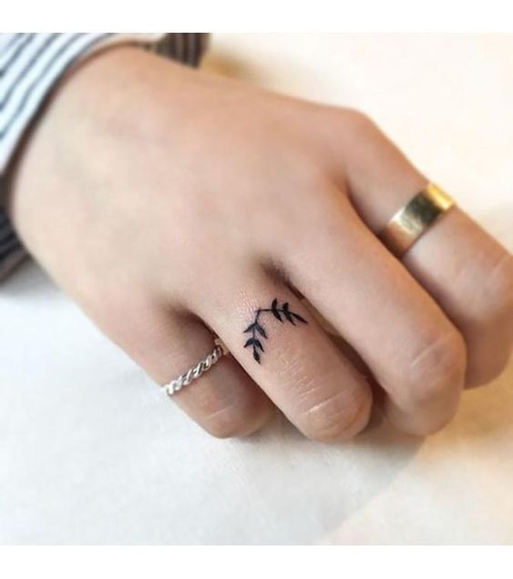 a person's hand with a small bird tattoo on the middle finger and an arrow ring