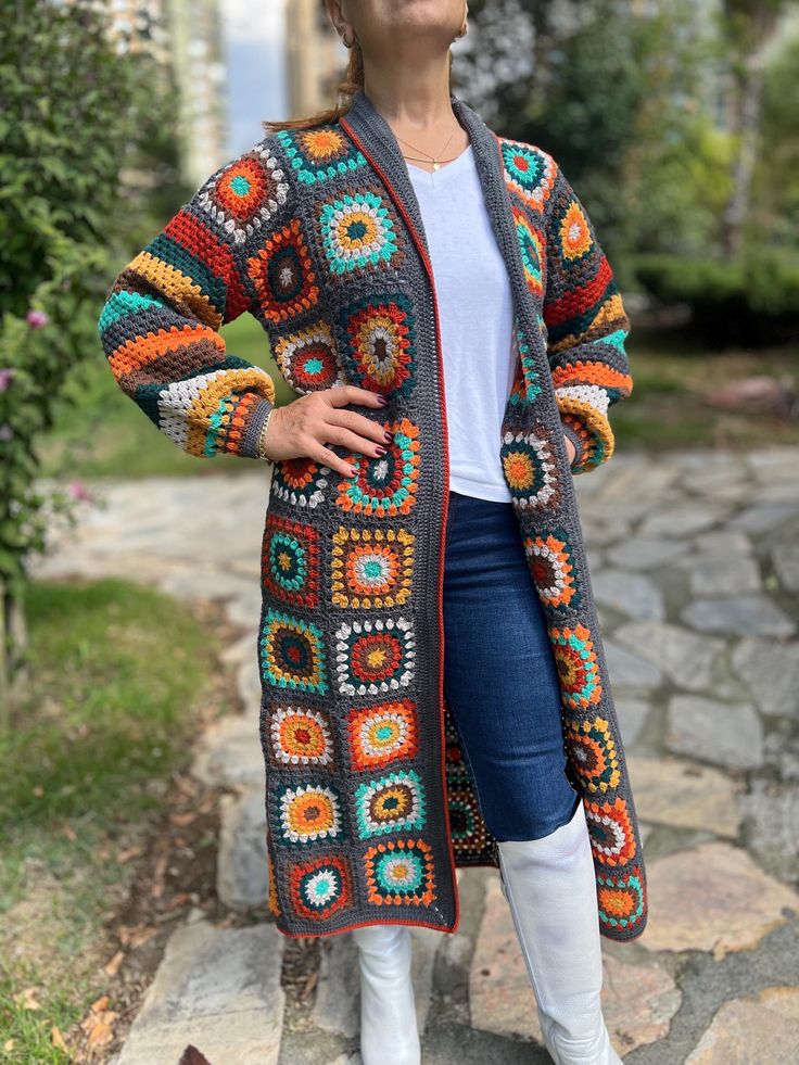 a woman is standing outside wearing a colorful crocheted cardigan