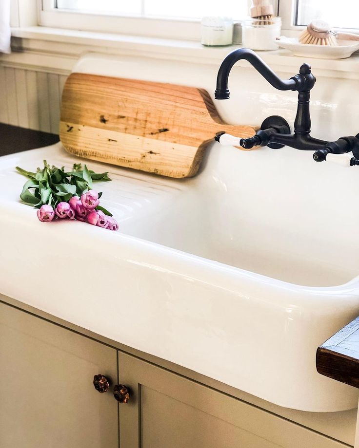 a white sink sitting under a window next to a wooden cutting board with flowers on it