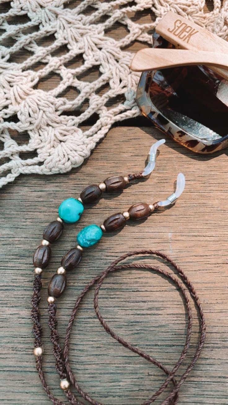 a necklace with beads and sunglasses on top of a wooden table next to a doily