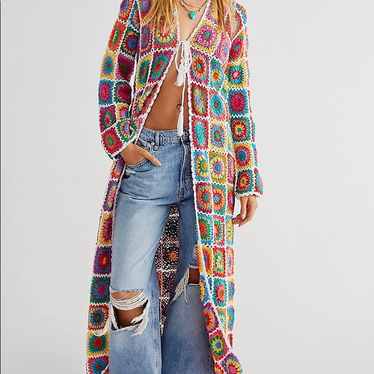 a woman wearing a colorful crochet cardigan and ripped jeans, standing in front of a white background